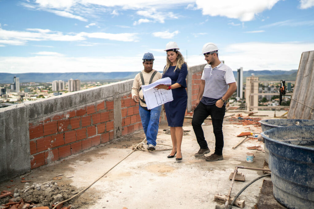 Engenheira e mestre de obras orientam pedreiro em obra.