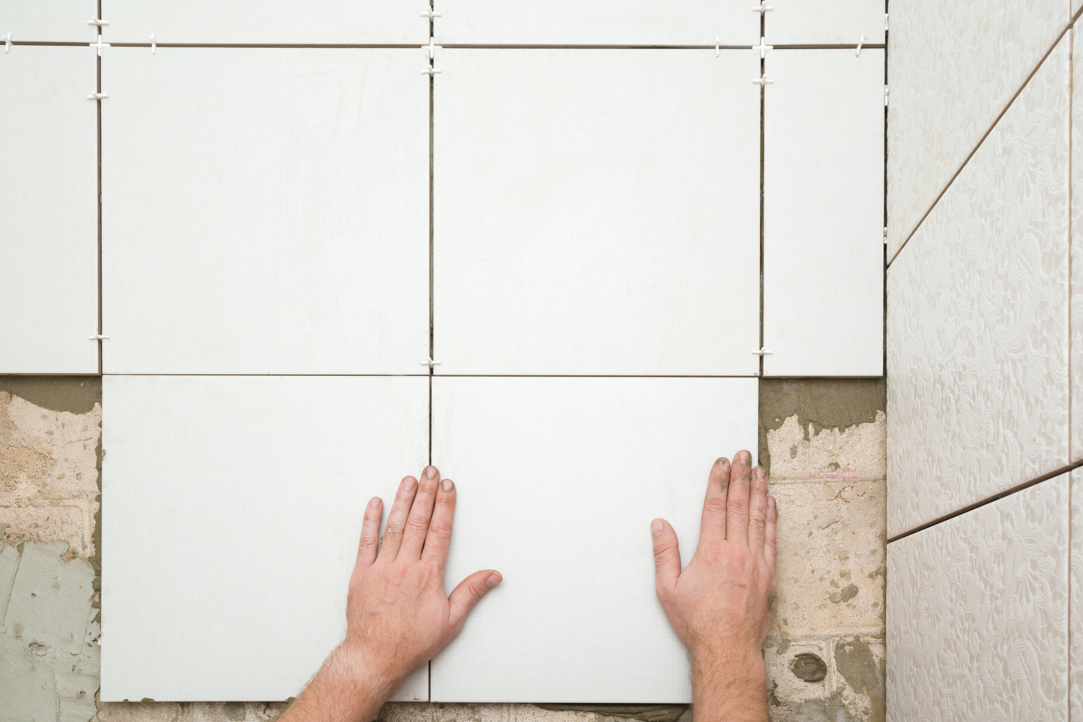 Mãos colocando uma cerâmica branca em um assentamento de piso em andamento.