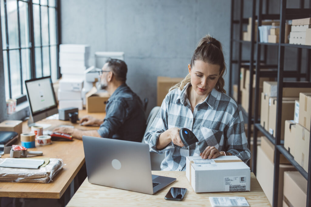 Dois empreendedores, um homem e uma mulher, organizam pedidos para serem despachados pelo e-commerce.