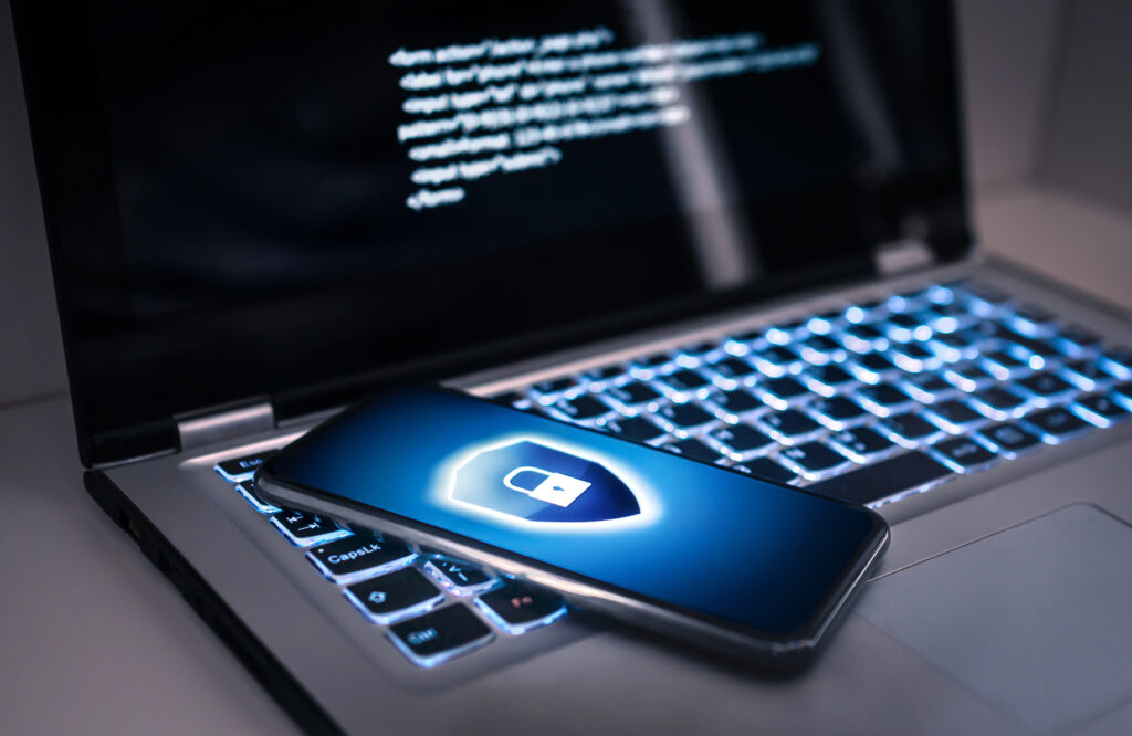 Notebook com um celular em cima, mostrando na tela um bloqueio telefônico para proteger contra golpe cibernético, fraude de dados online ou roubo de identidade.
