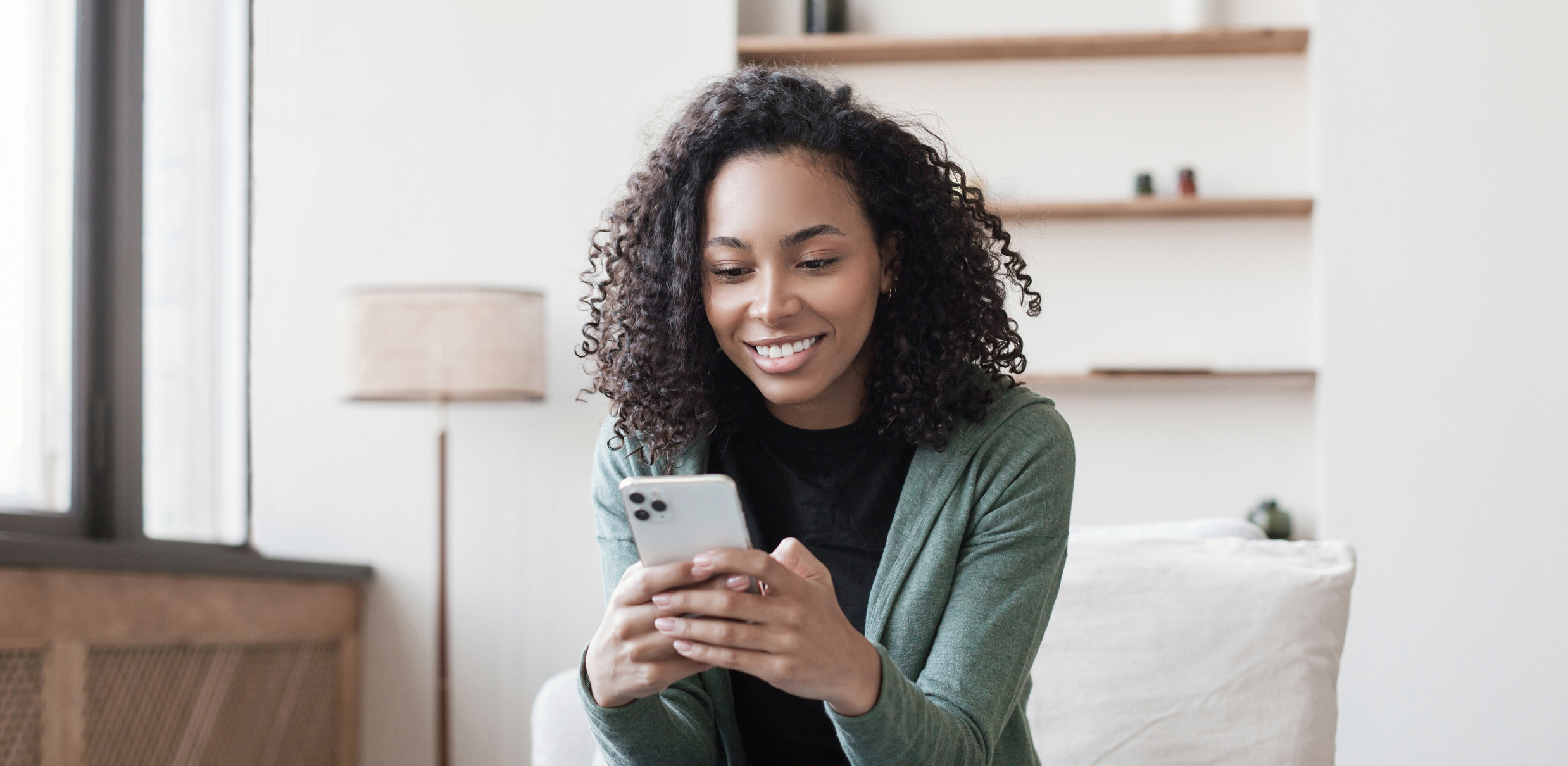 Mulher mexendo em smartphone e sorrindo para a tela.