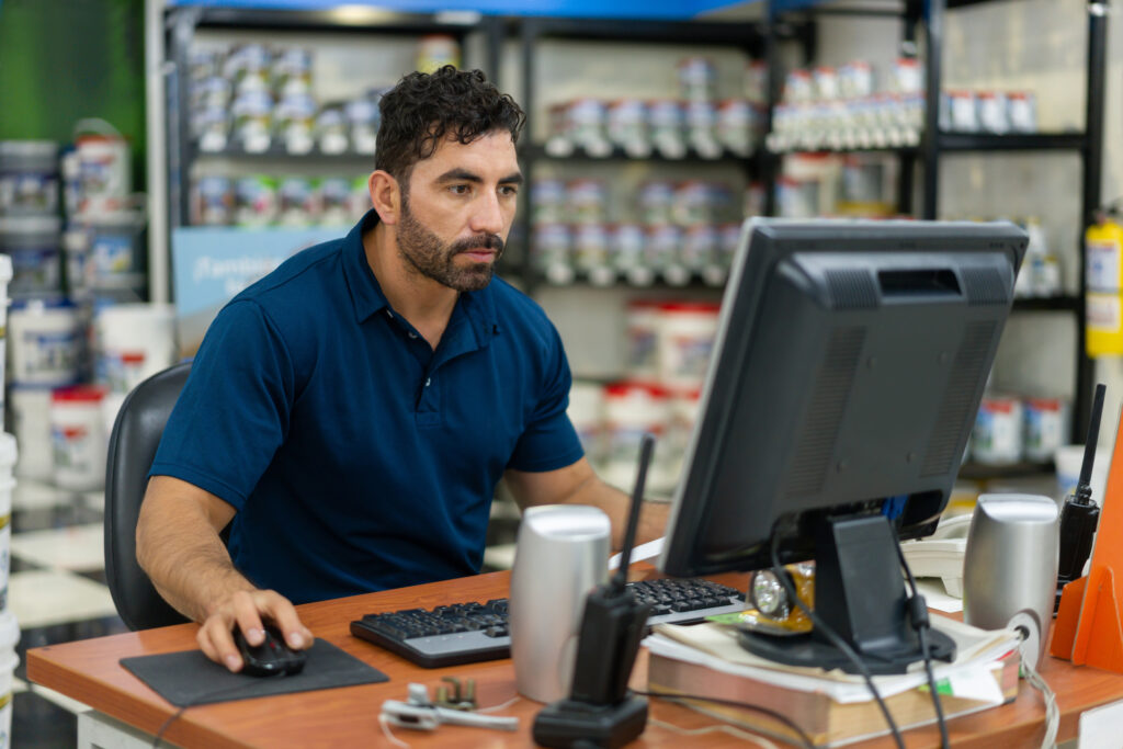 Gerente de negócios usando um computador portátil em uma loja de materiais de construção. Ele é um homem branco de meia idade que está concentrado.