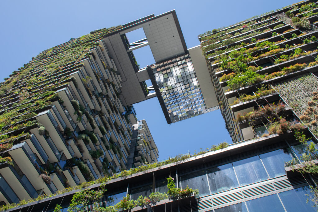 Foto de um edifício de arquitetura moderna com a fachada repleta de plantas, representando o conceito de construções sustentáveis