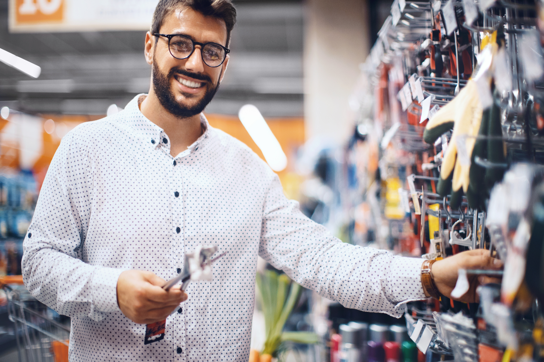 Cliente de loja de material de construção comprando ferramentas de trabalho profissional. Ele é um homem branco, jovem, de barba e está sorrindo