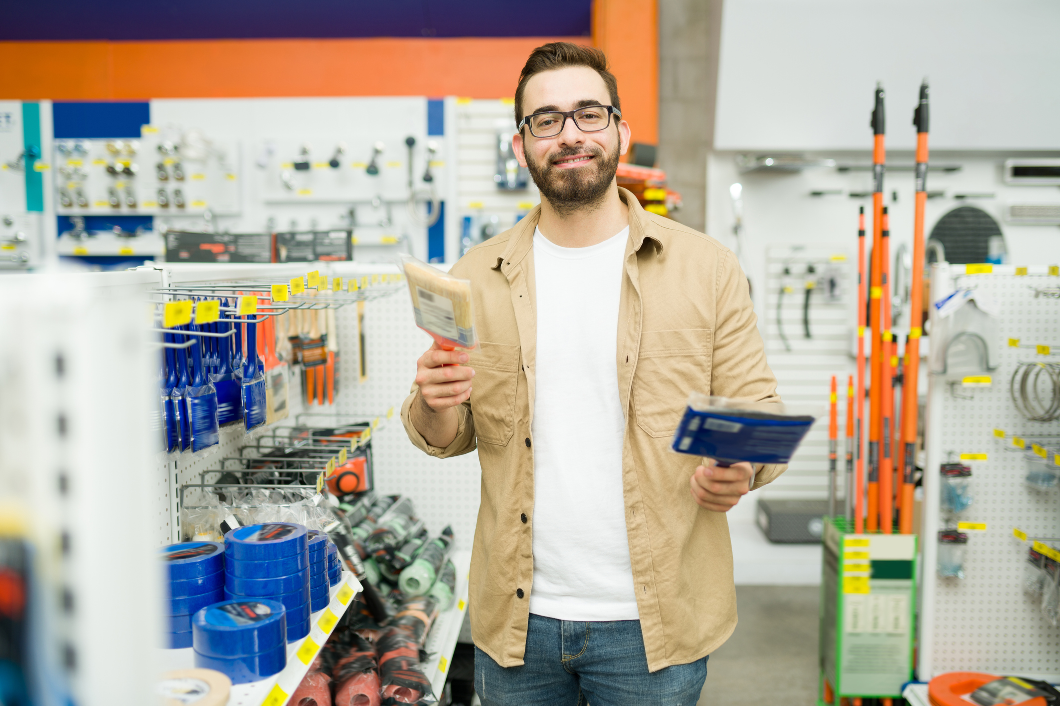 Jovem feliz decidindo comprar um pincel na loja de ferragens, ele é um homem branco que segura dois pinceis