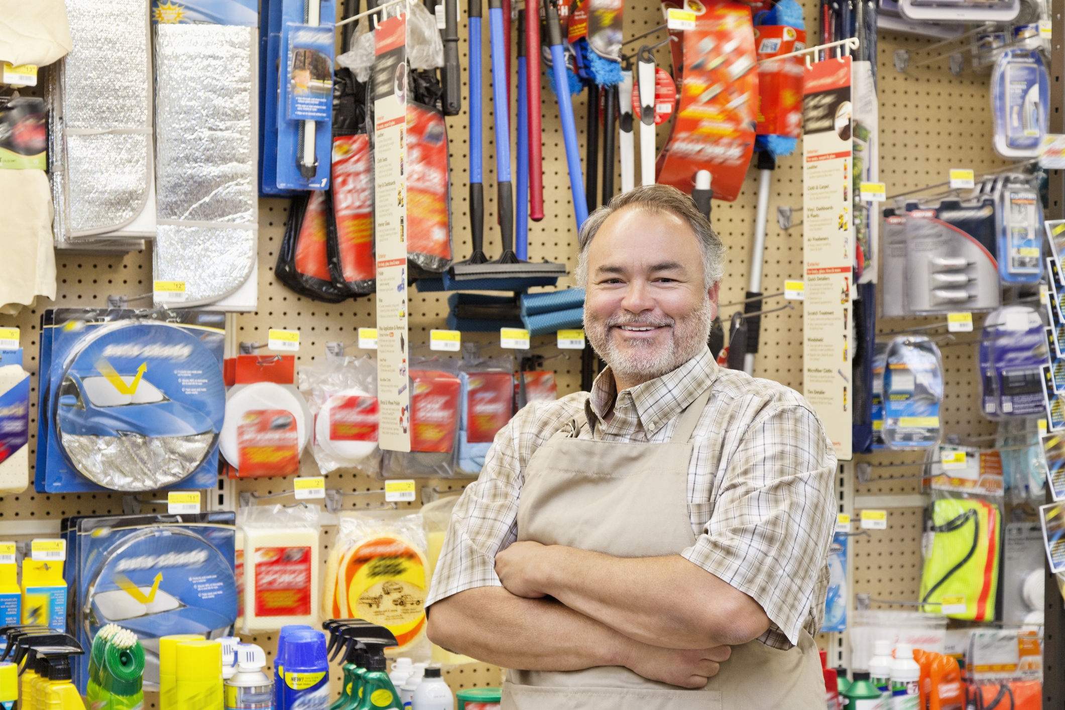 Vendedor de loja de material de construção posa sorrindo entre as prateleiras, ele é um homem branco, de meia idade, com barba e cabelos grisalhos.